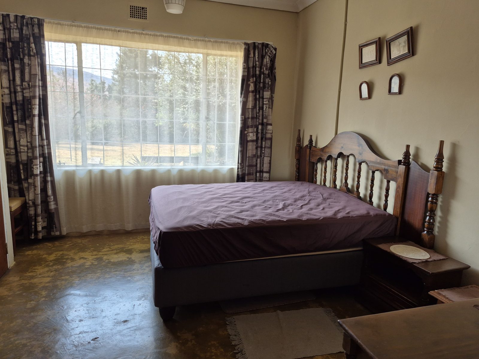 Main bedroom with a wooden headboard and a wide window onto the lawn