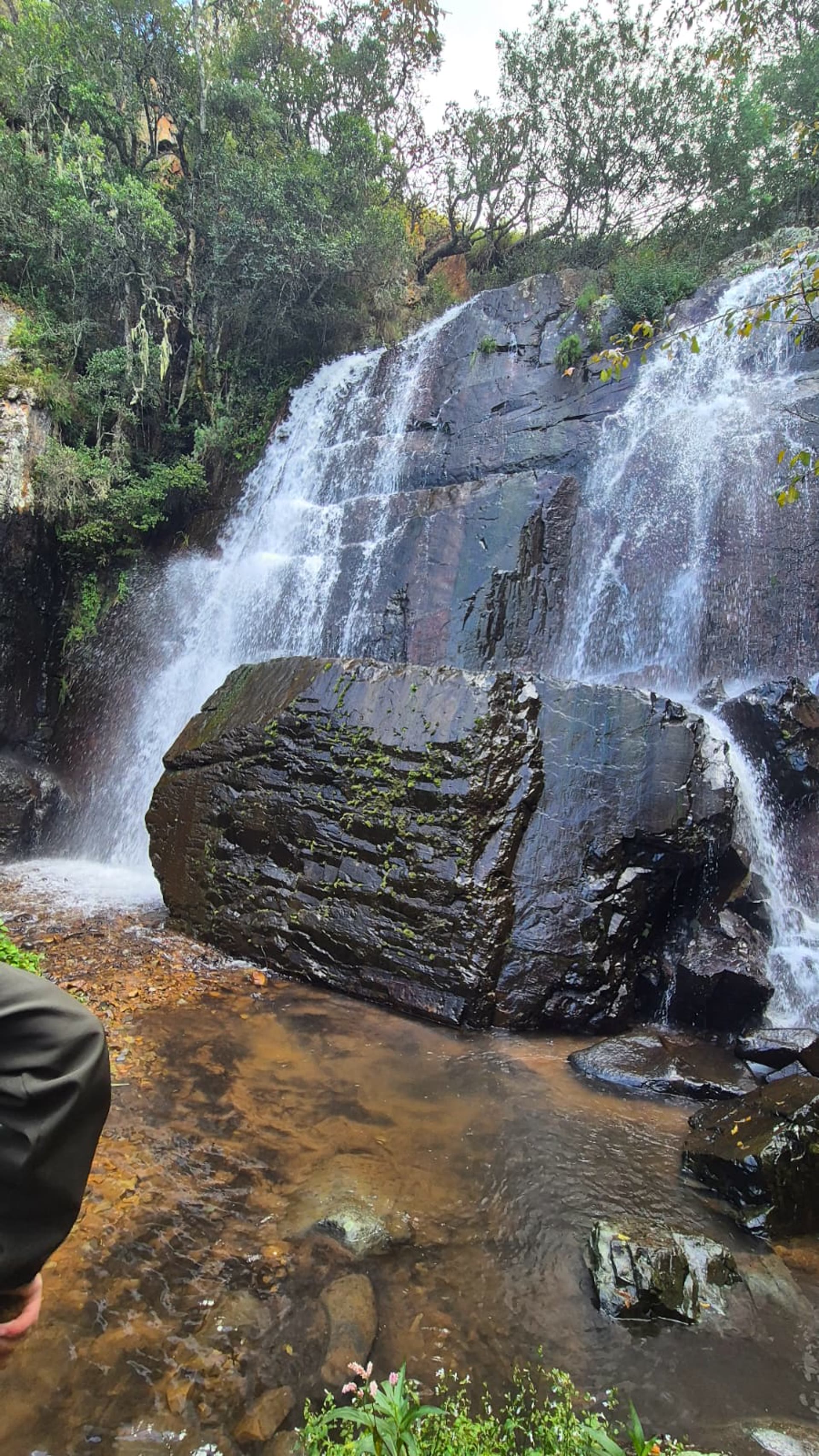 The big waterfall pouring over dark rock around a huge mossy boulder